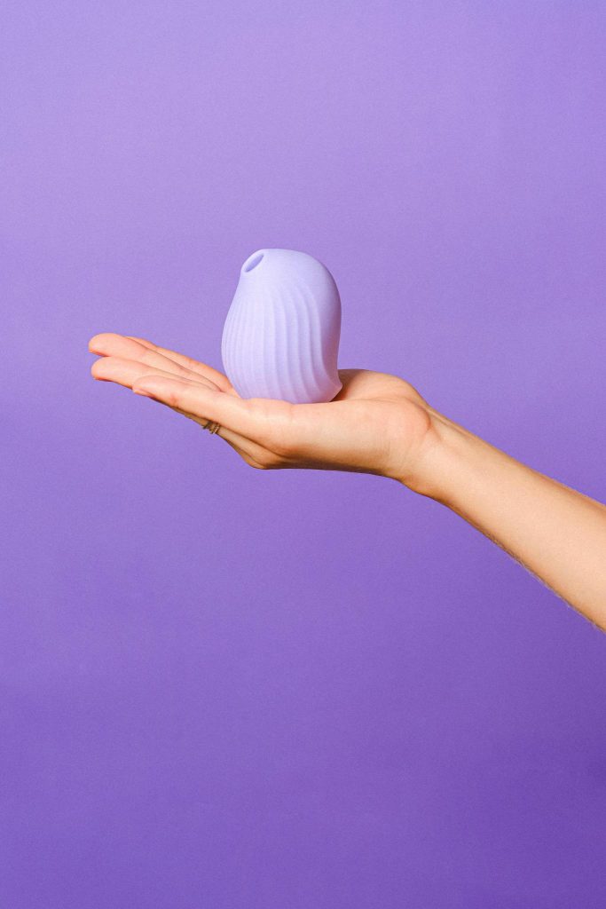 A minimalist image of a silicone toy held on an open hand against a bright purple backdrop.