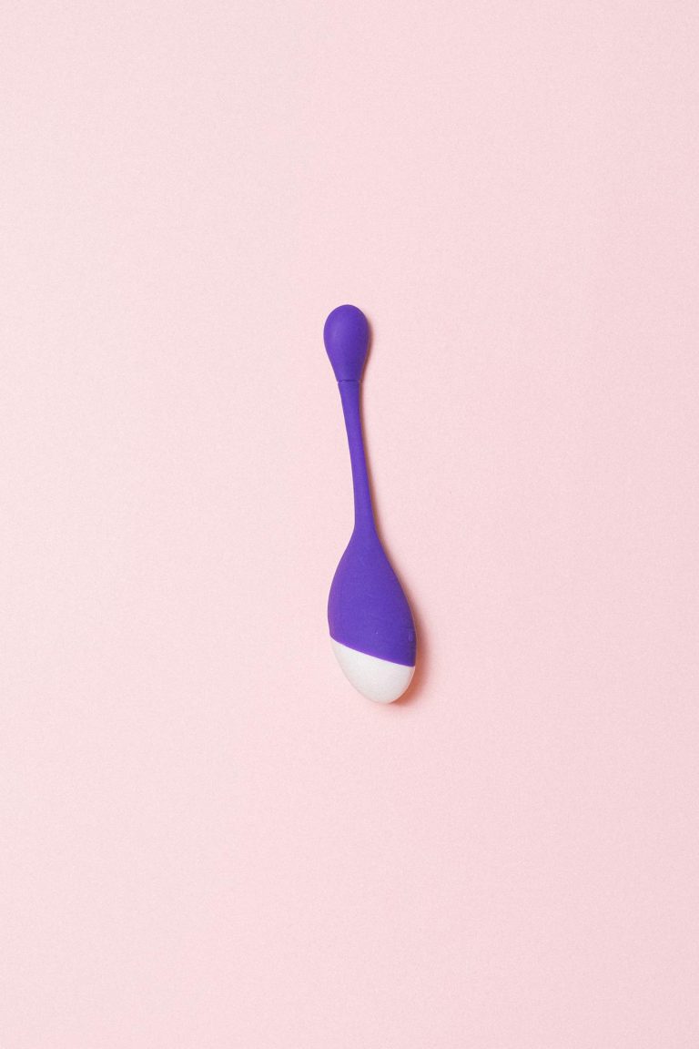 Minimalist photo of a purple silicone sex toy on a light pink background.
