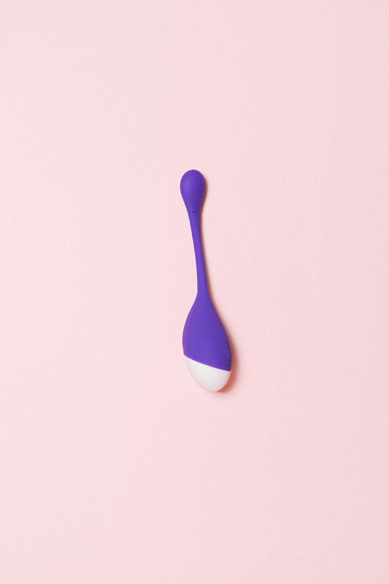 Minimalist photo of a purple silicone sex toy on a light pink background.